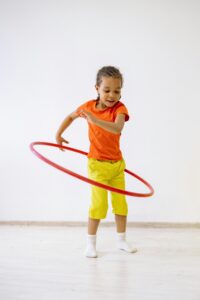 Energetic young girl hula hooping indoors in bright attire, enjoying playtime.